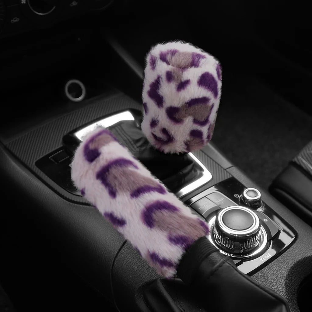 Car handbrake and gear shift cover with purple and white leopard print design on a black car interior background.