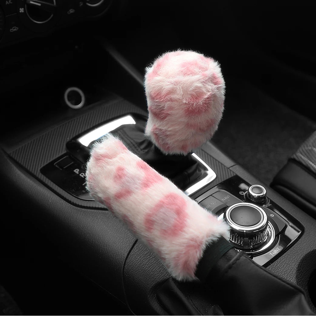 Car handbrake and gear shift cover with fluffy pink design on a car dashboard.