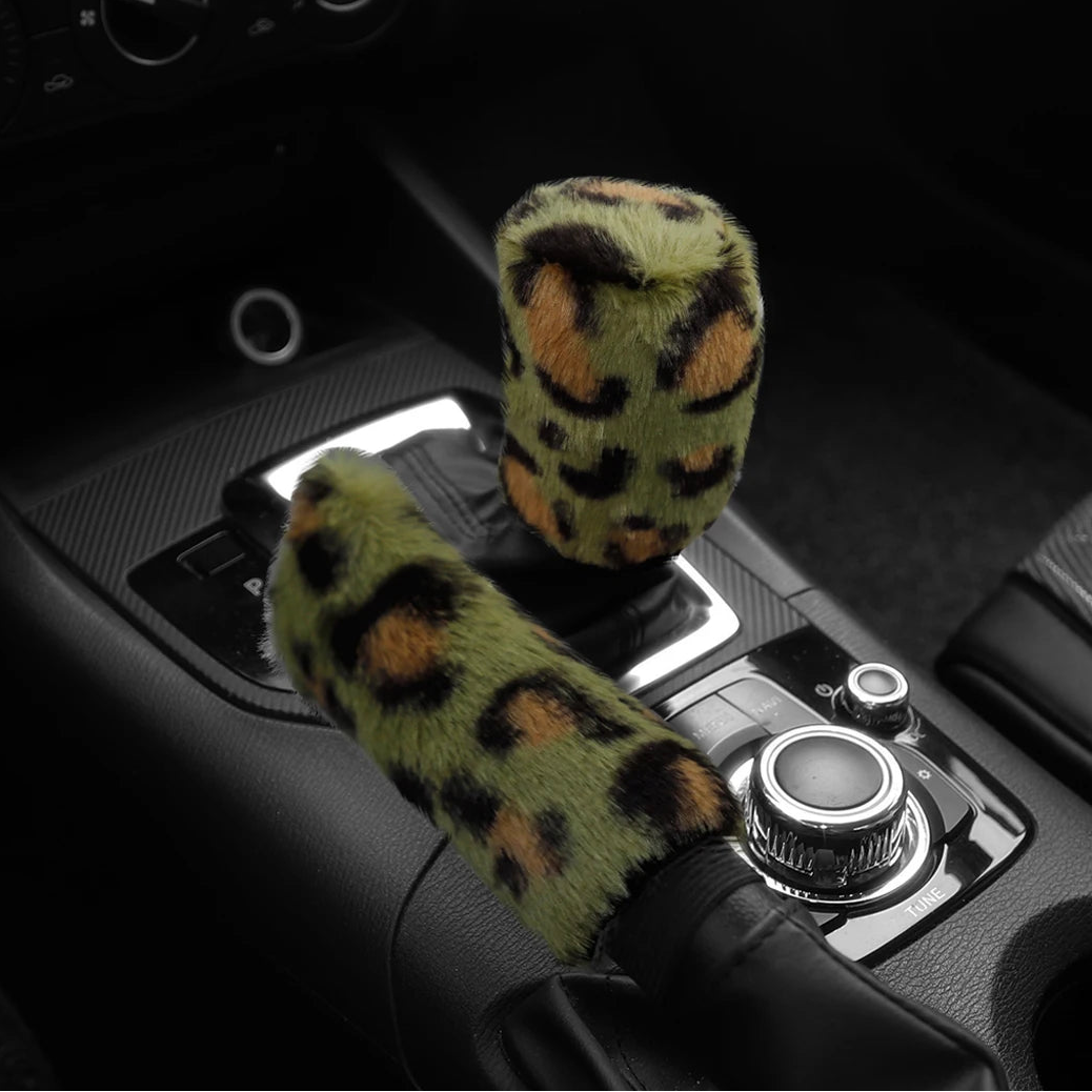 Car handbrake and gear shift cover with green leopard print design on a black car interior background.